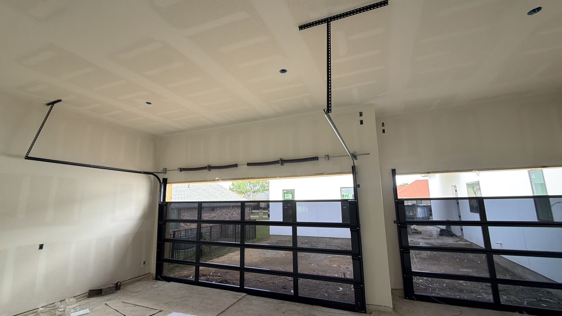Two glass garage doors with new tracks, springs, and opener rails in a new construction garage
