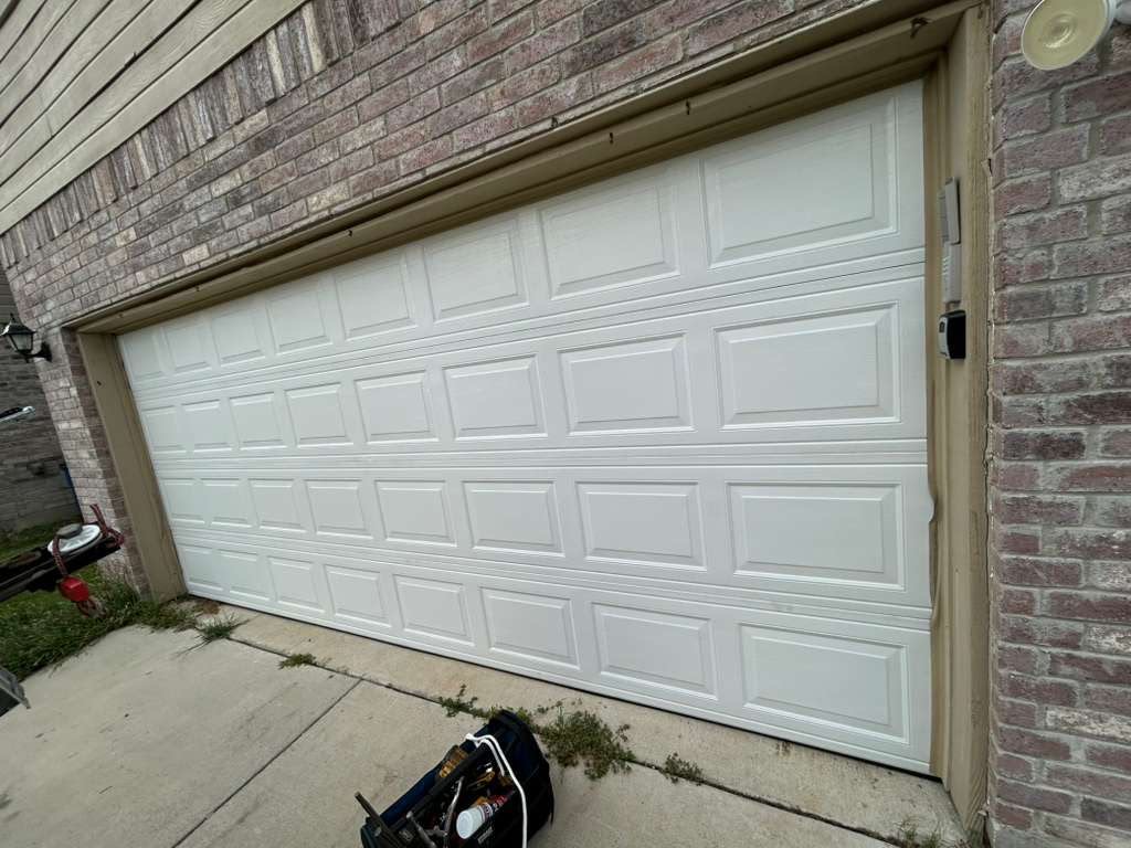 New white short-panel garage door installed on a brick home with tool bag on the driveway