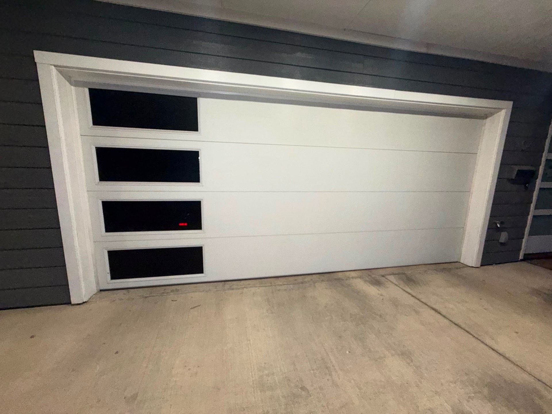 New white modern garage door with black window inserts installed on a dark home